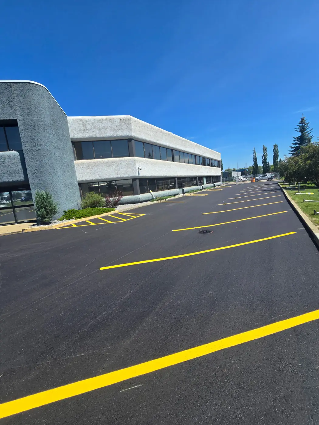 Same parking lot after repaving — new asphalt and yellow line painting