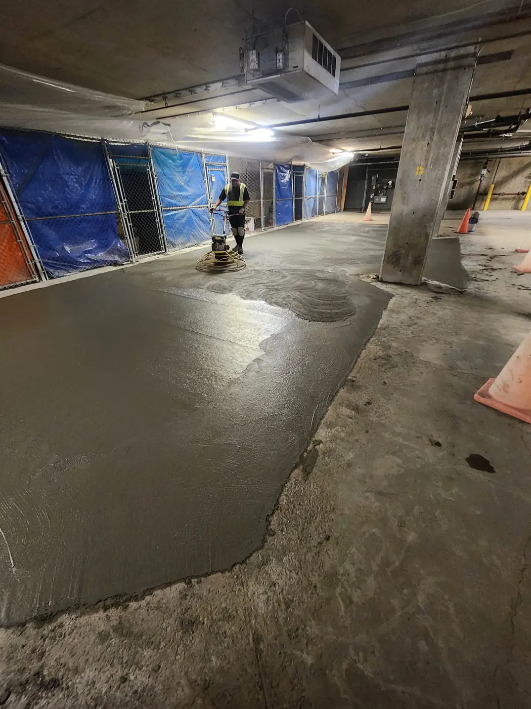 Worker power-troweling a new concrete slab in an underground parkade