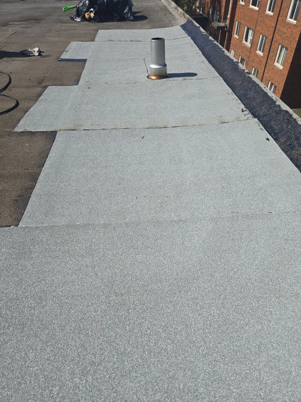 New granulated roofing membrane being installed on a flat roof beside a brick building